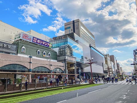 現代的な店舗やビルが立ち並ぶ賑やかな通りの都市風景。路面電車の停留所と歩行者が特徴的な街の光景。
