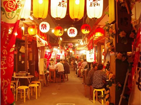 飲食店が立ち並び、提灯が灯る日本の夜の路地。食事を楽しむ人々で賑わっています。